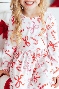 Girl wearing white long sleeve twirl dress with red candy cane, bow, and snowflake print. Perfect festive outfit for holidays.