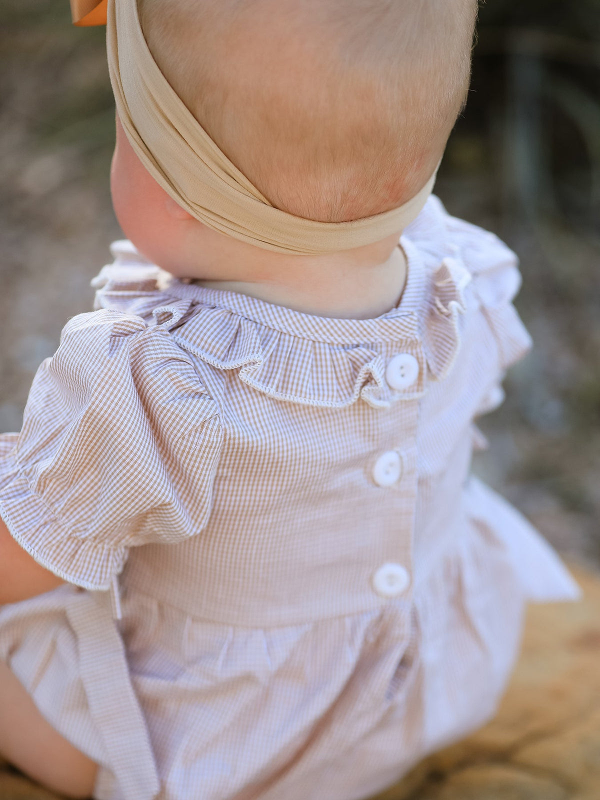 Back view of a baby wearing a plaid smocked romper with ruffled sleeves and white buttons.