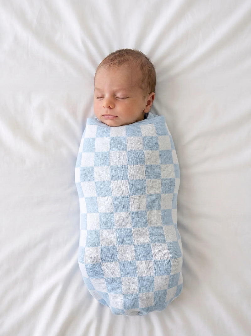 Newborn baby swaddled in light blue and white checker patterned knit blanket on soft white textured bed sheet