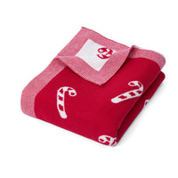 Folded red baby blanket with white candy cane motif and turned back white corner