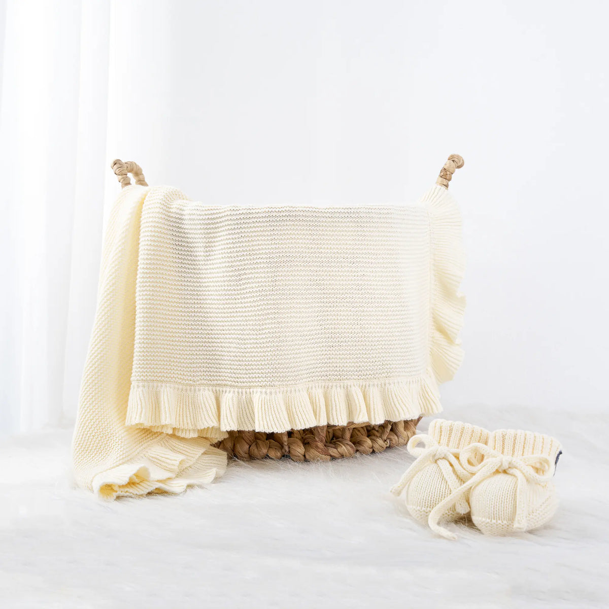 Cream knitted baby receiving blanket draped over seagrass basket with matching booties