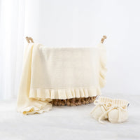 Cream knitted baby receiving blanket draped over seagrass basket with matching booties
