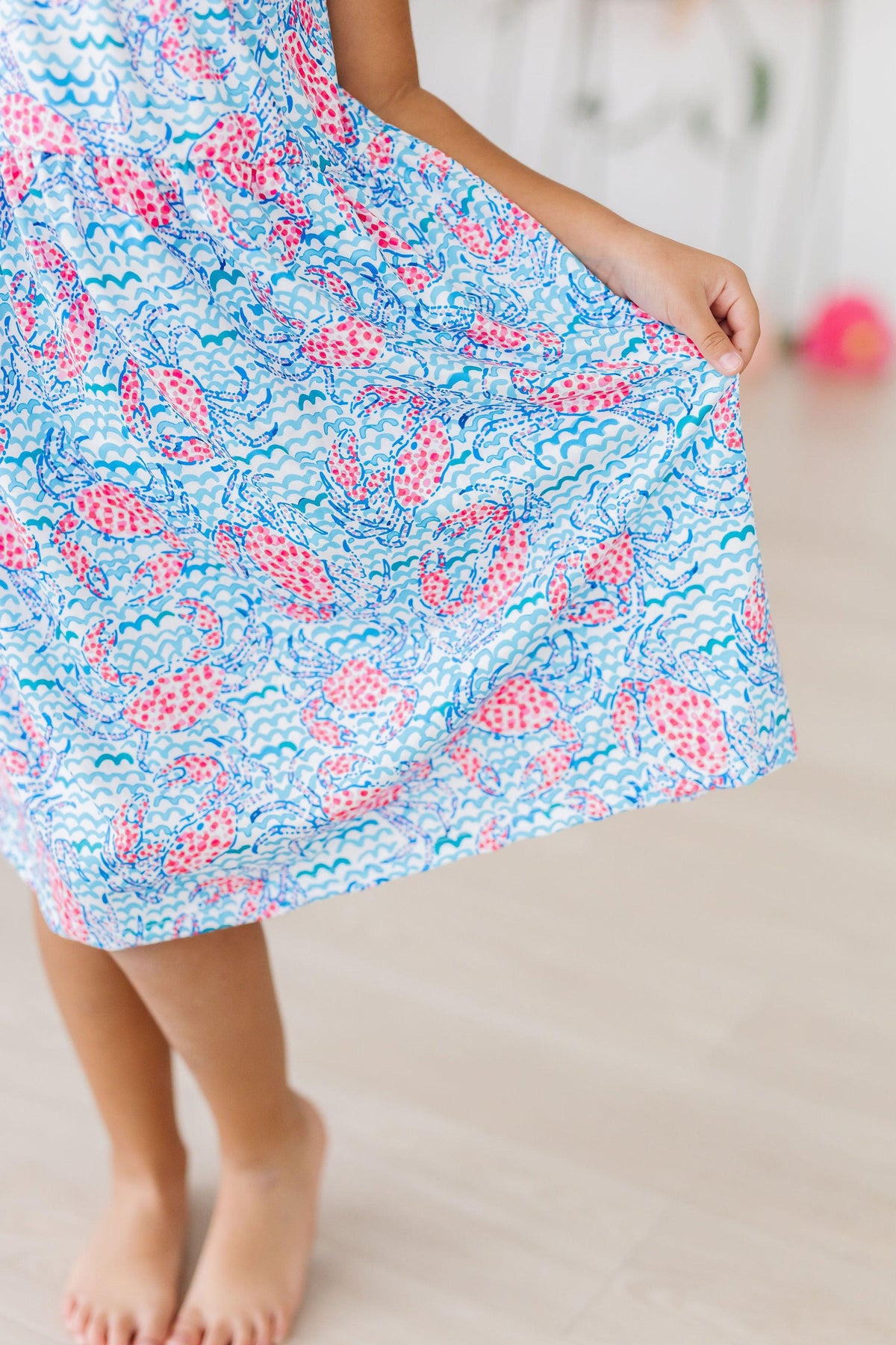 A little girl wearing the Crab Walk Ruffle Cross Back Dress, demonstrating its comfortable fit and adorable beachy style.
