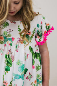 Cute Cactus Pom Pom Dress by Mila & Rose on a girl, white fabric with cactus print and pink pom-pom sleeve trim.