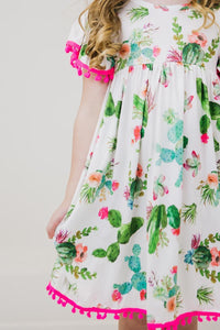 Cute Cactus Pom Pom Dress, white fabric with cactus and floral print, pink pom pom trim.