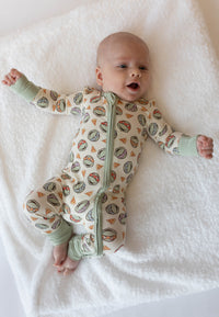 Infant in cream TMNT print bamboo onesie lying on white blanket with sage green cuffs