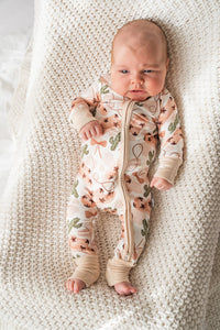 Baby in cowgirl print bamboo baby loveralls with cactus pattern lying on white knit blanket