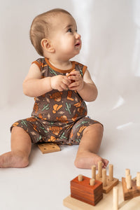 Baby in brown highland cow baby romper with orange trim holding wooden block