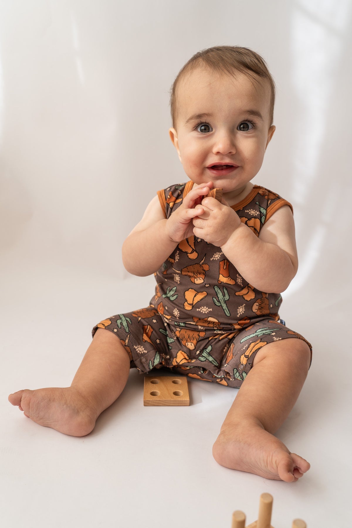 Smiling baby in organic bamboo shorty romper with leg snaps and wood toy