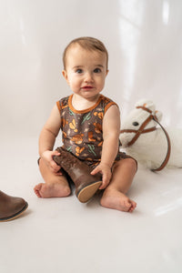 Infant wearing western print onesie holding miniature cowboy boot toy