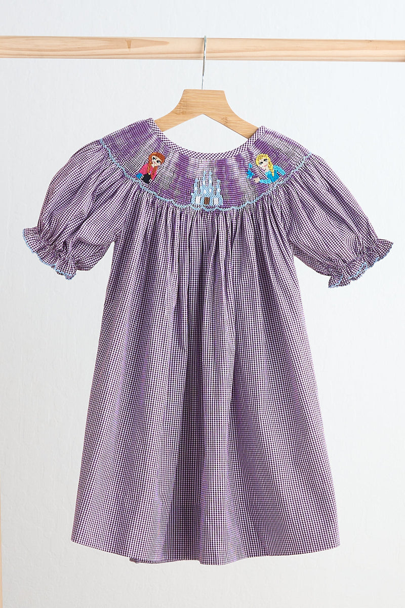 Purple checkered dress with embroidered designs on a wooden hanger against a white background