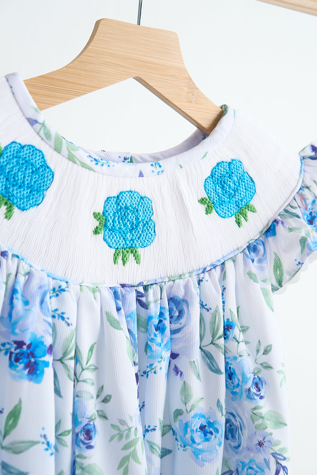Blue rose hand smocked print dress featuring embroidered floral collar and bishop silhouette on wooden hanger