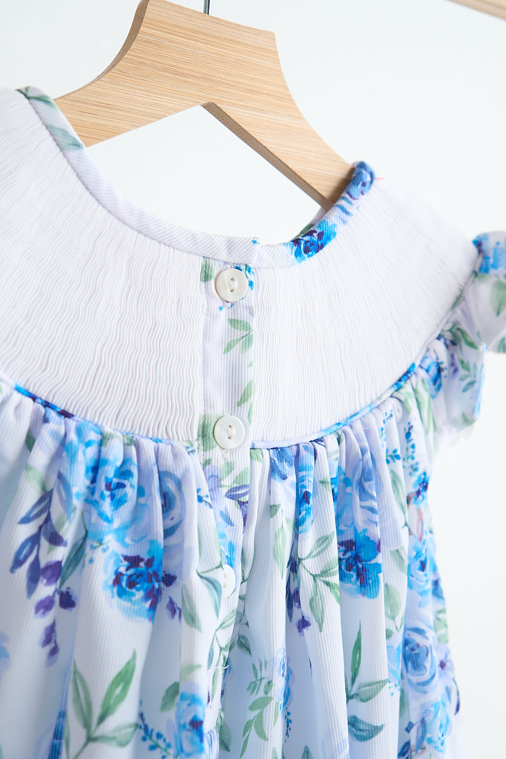 Blue rose hand smocked print dress featuring white shirred bodice, button detail, and breathable floral bishop silhouette for girls.