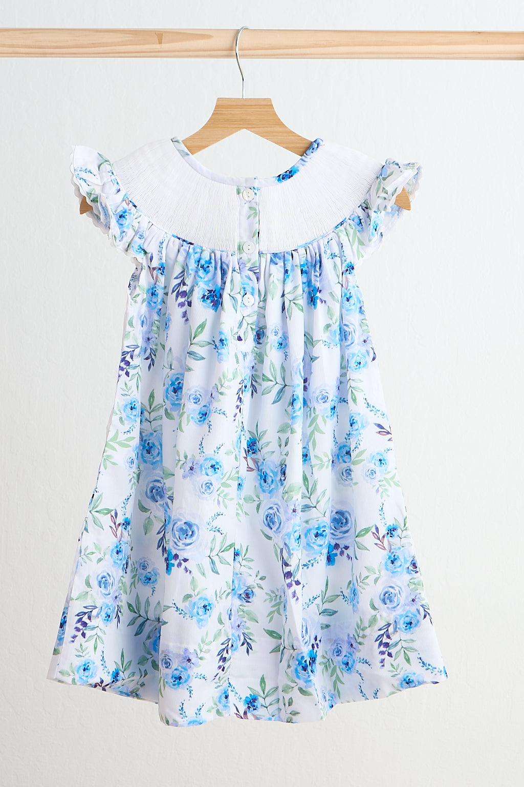 Blue rose hand smocked print dress with white gathered collar and ruffled sleeves on a wooden hanger.