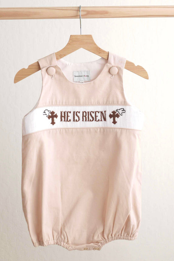 Baby romper with 'He is Risen' text on a hanger against a plain background