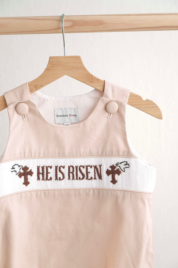 Baby dress with 'He Is Risen' text on a hanger against a white background