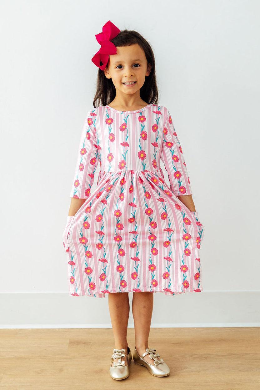 A happy girl wearing the Daisy Chain Three Quarter Sleeve Pocket Twirl Dress with pockets, designed for fun and movement as a stylish girls pocket twirl dress.