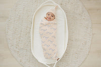 Smiling baby swaddled in GOTS certified organic cotton Dalmatian blanket inside oval bassinet on woven rug.