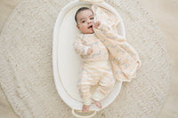 Baby holding a soft peach Dalmatian print organic cotton blanket in a white bassinet on a textured rug.
