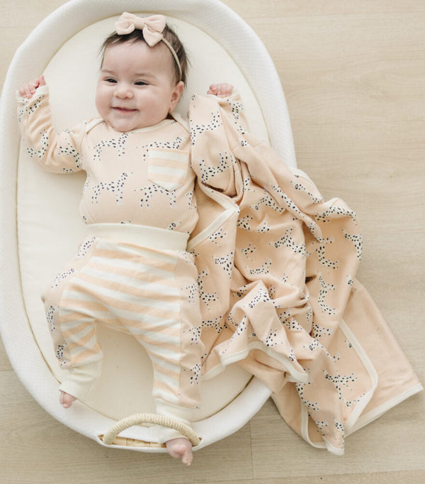 Smiling baby in Dalmatian print outfit lies in Moses basket with matching GOTS certified organic cotton blanket.