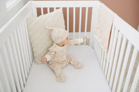 Baby in Dalmatian print organic cotton pajamas and hat reaches for matching GOTS certified blanket draped on white crib rail.