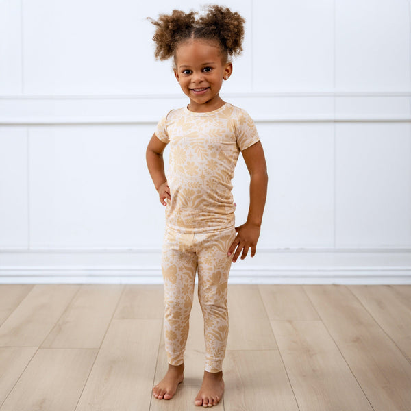 Child wearing beige two-piece short-sleeve pajama set with botanical print.