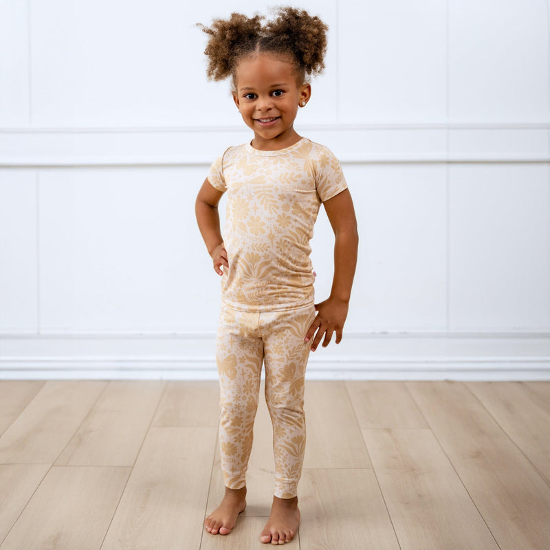 Child wearing beige two-piece short-sleeve pajama set with botanical print.