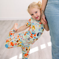 Child in The Second-Skin 2-Piece Short Sleeve Pajama by Mindful Doggos, colorful hand-drawn print, with caregiver.