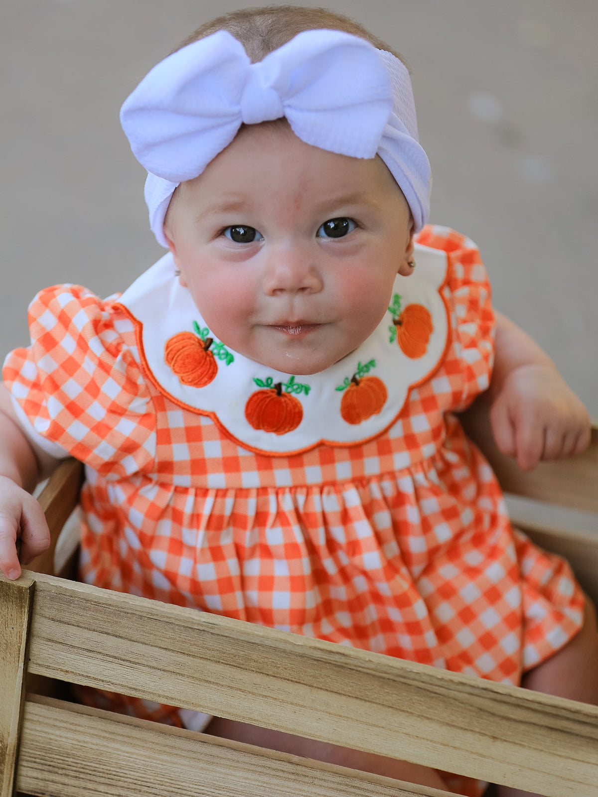 Orange gingham puff sleeve baby romper with pumpkin applique Peter Pan collar, bloomers, and white bow headband for Halloween or Thanksgiving.