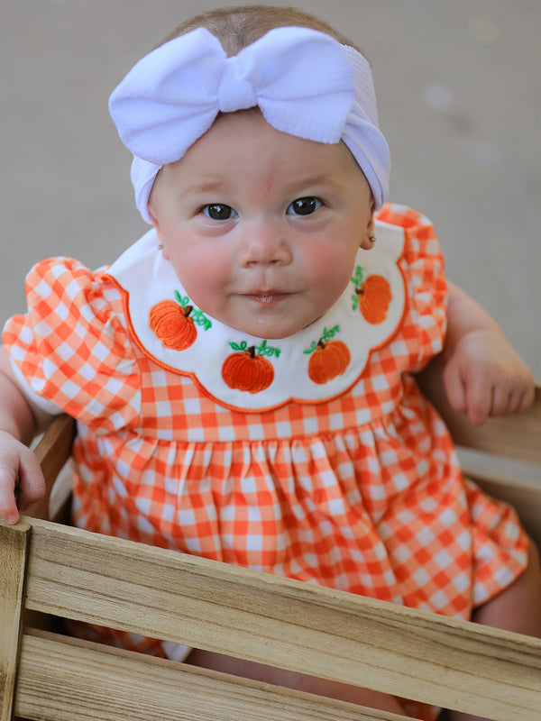 Orange gingham puff sleeve baby romper with pumpkin applique Peter Pan collar, bloomers, and white bow headband for Halloween or Thanksgiving.