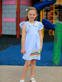 Girl wearing pastel blue striped crayon twirl dress with a petal collar and colorful hem applique at a playground.