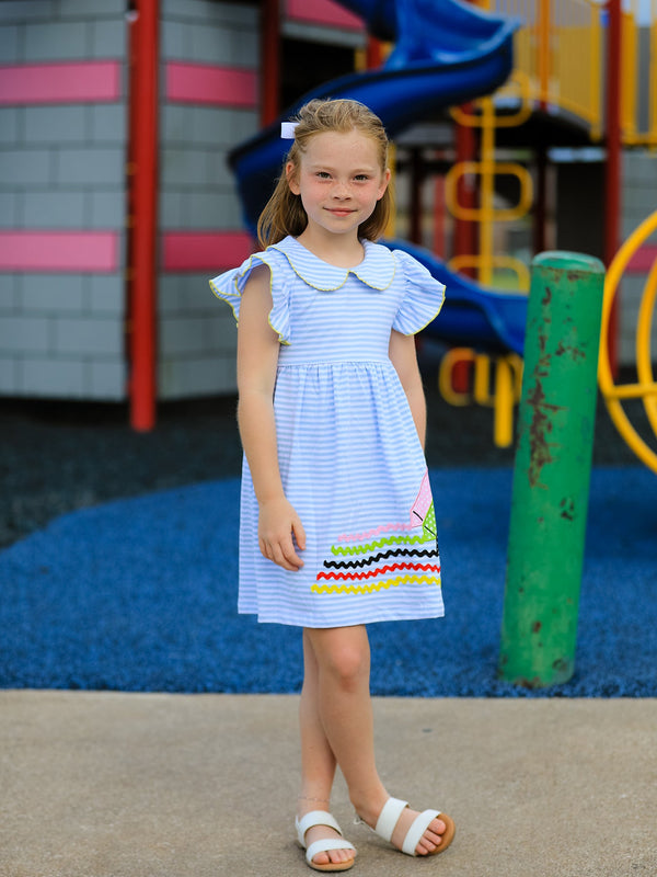 Girl in Back To School Crayon Dress with ruffle sleeves and petal collar at playground