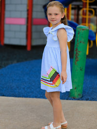 Girl wearing back-to-school crayon dress with blue stripes, ruffle petal collar applique and colorful details.