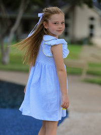 Girl in back-to-school blue striped dress with ruffle sleeves and white hair ribbon outdoors.
