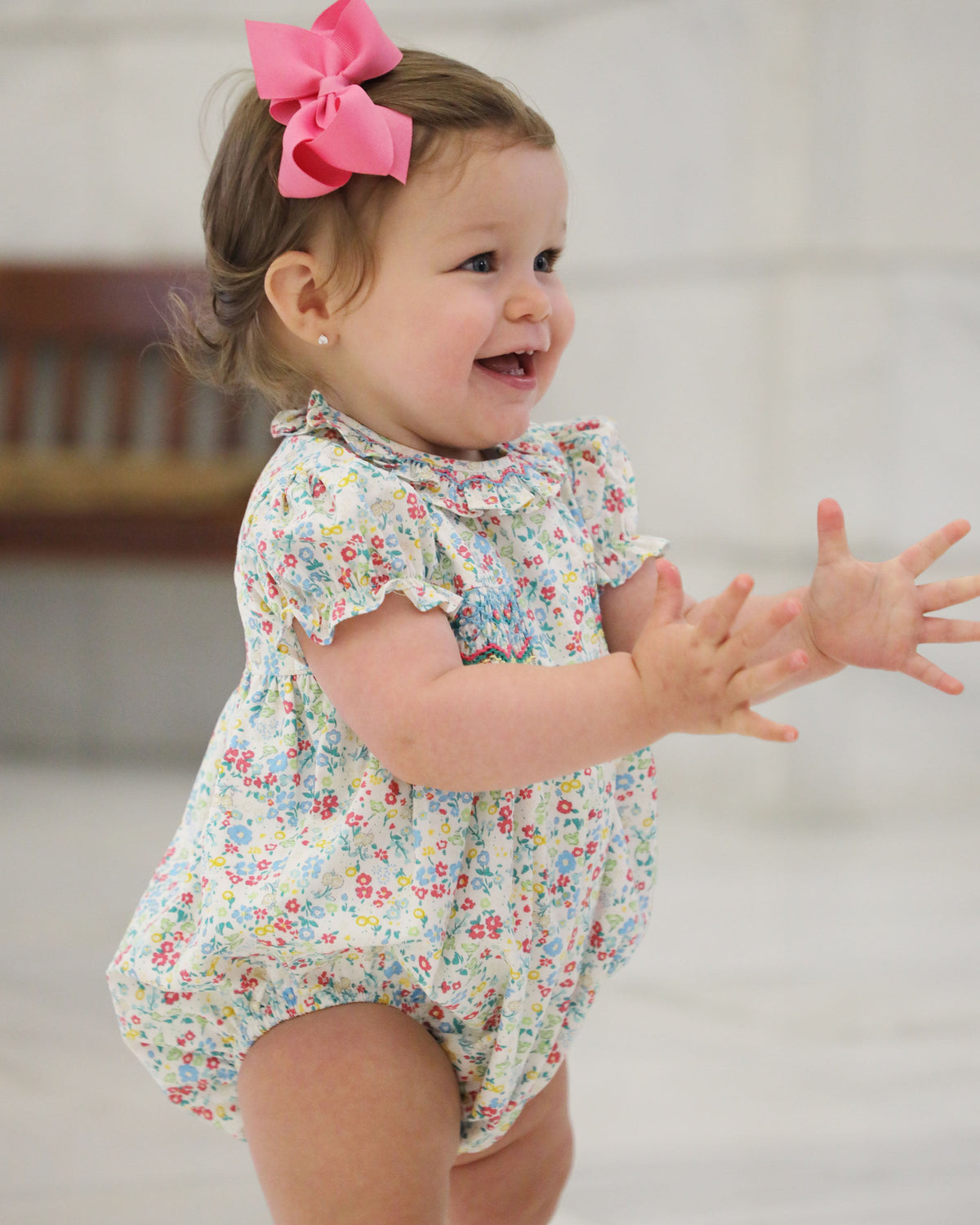 Baby standing reaching out in loose fitting floral romper showing movement of ruffled sleeves