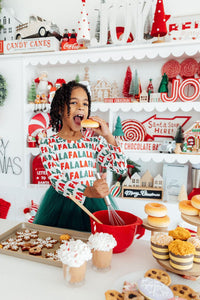 Little girl in a Fa La La long sleeve tutu dress baking holidays treats. Festive ballerina outfit with green tulle skirt, perfect for holiday season play.