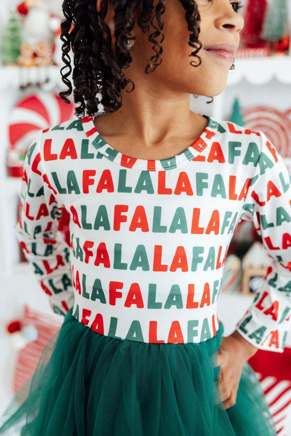 Girl wearing white long sleeve dress with red and green "Fa La La" print and emerald green tutu skirt.