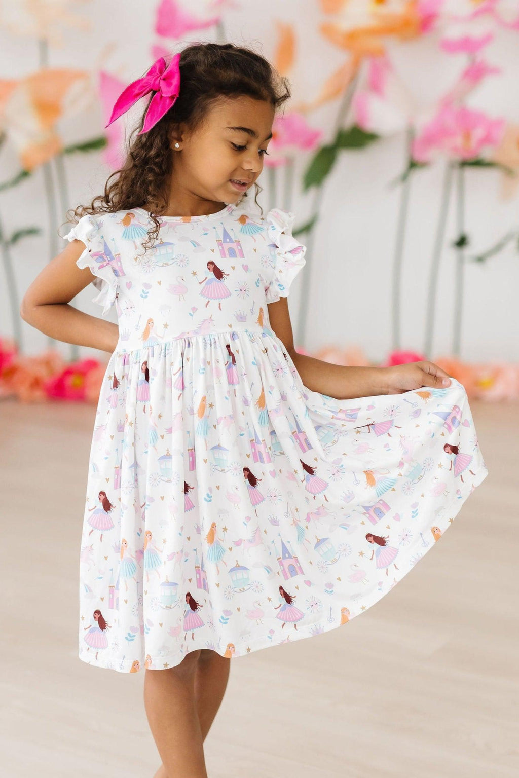 Girl wearing the Fairy Princess Flutter Sleeve Twirl Dress, twirling joyfully in a bright, cheerful setting with floral decorations.
