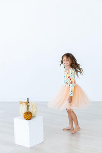 Smiling girl twirling in a fall watercolors long sleeve tutu dress with a peach skirt and woven pumpkin decor.