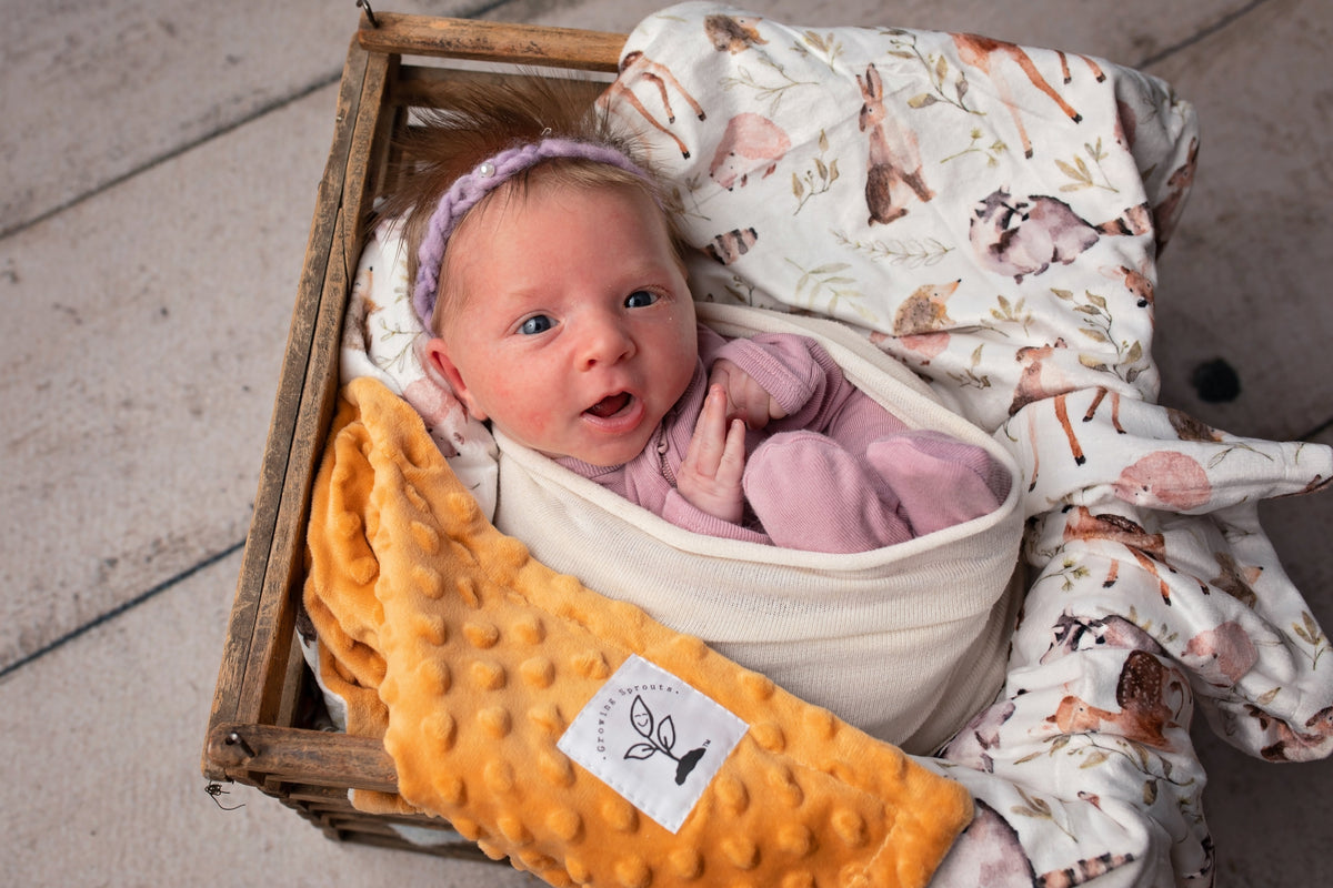 Baby nestled in orange minky dot blanket and watercolor forest animal print swaddle. Soft, hypoallergenic, and durable nursery essential.