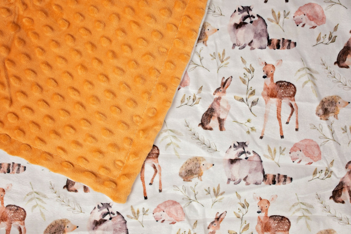 Soft orange minky blanket with watercolor forest animals including deer, raccoons, and hedgehogs on a white background.