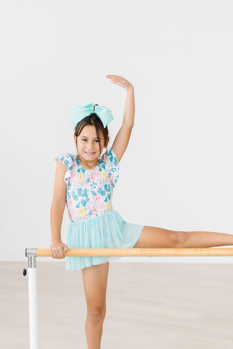 A girl performing a graceful pose in the Floral Garden Short Sleeve Twirl Leotard for Girls, emphasizing the playful twirl design.