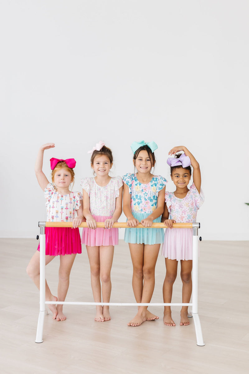 Four girls in colorful Floral Garden Short Sleeve Twirl Leotards for Girls, each with a unique style, gathered by the ballet barre.
