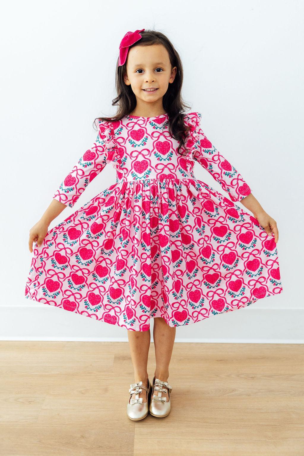 Toddler twirling in pink heart print 3/4 sleeve ruffle dress. Comfortable, easy-wash twirl gown designed for play and special occasions.