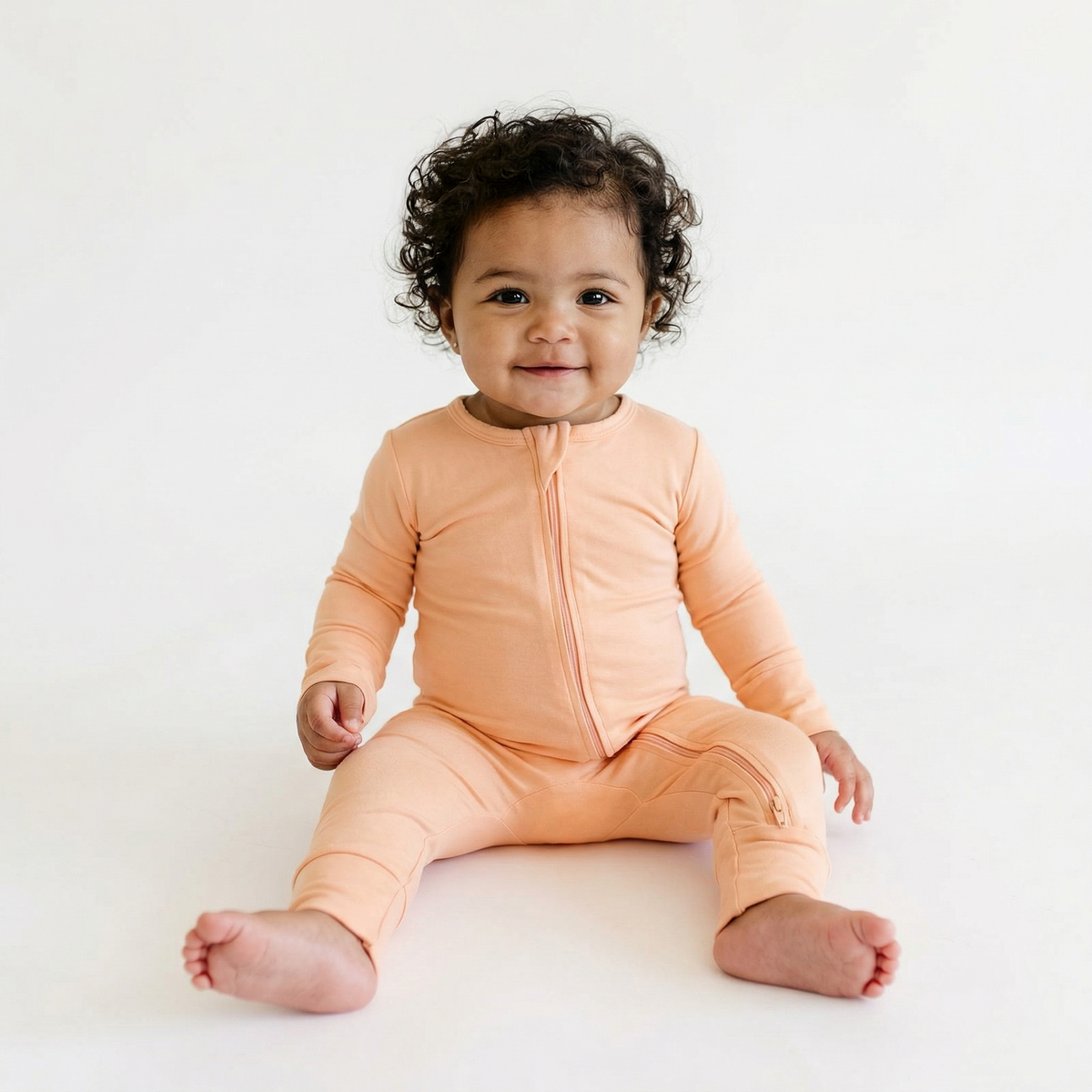 Baby wearing peach fuzzy convertible footie pajamas on white background