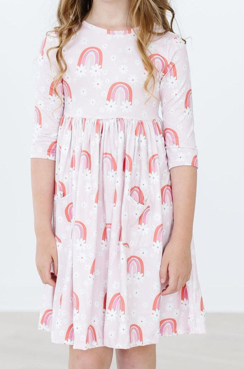 Close-up view of the Fun & Flowers 3/4 Sleeve Pocket Twirl Dress, showcasing its delightful rainbow pattern and a young girl ready for fun and adventure.