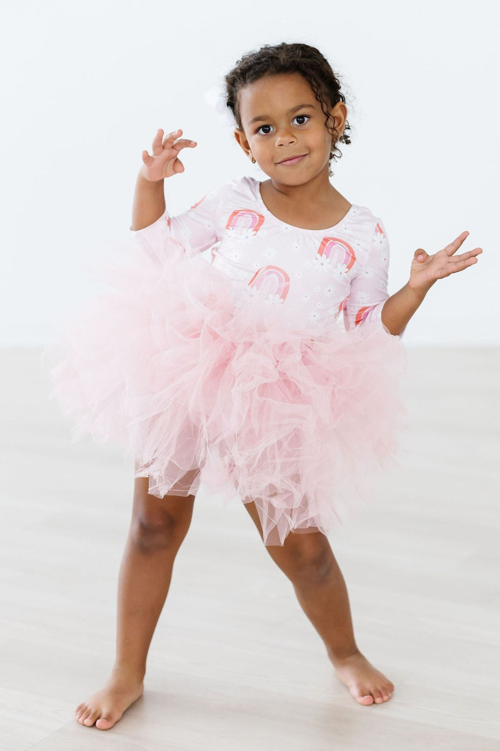 Fun & Flowers 3/4 Tutu Leotard featured on a young girl with curly hair posing with playful gestures, showcasing the vibrant floral design and fluffy pink tutu.