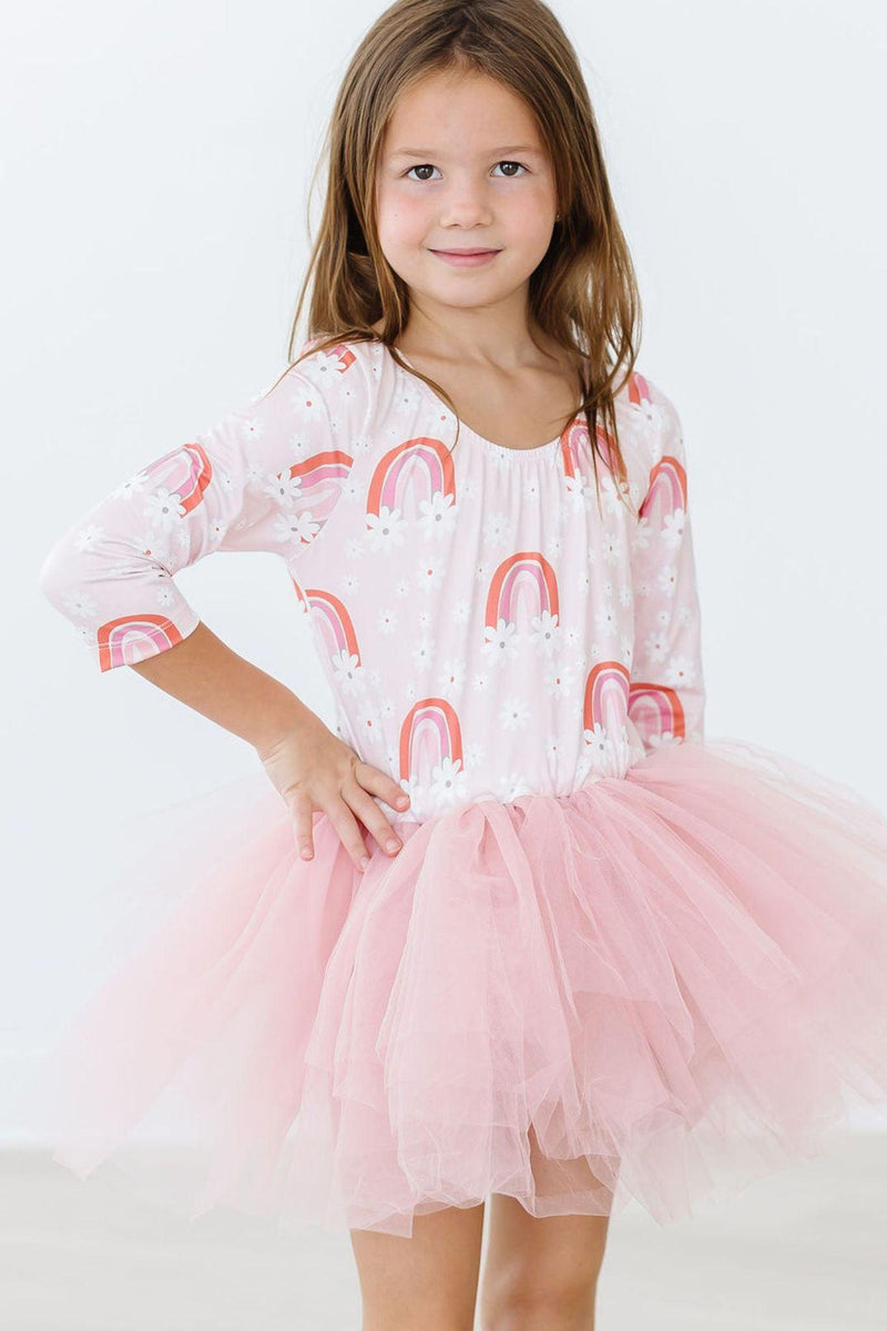 Young girl wearing the Fun & Flowers 3/4 Tutu Leotard, proudly standing with hands on hips, highlighting the enchanting rainbow and floral pattern.