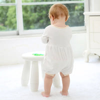 Back view of a toddler wearing a white special occasion romper with button-back closure, suitable for formal events.