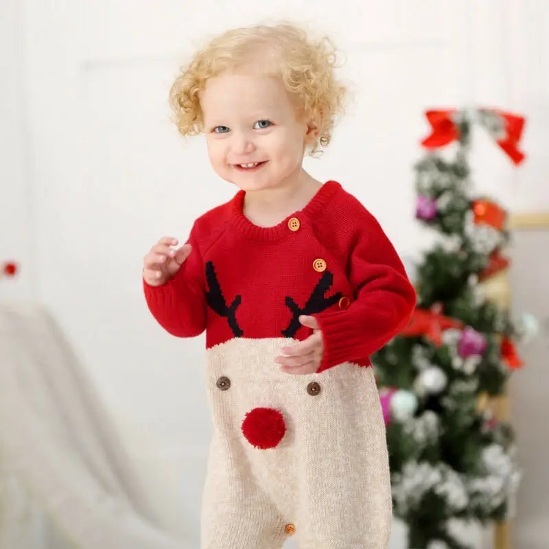 Happy toddler in Rudy Reindeer Knit Children's Winter Romper in red, playing in a festive atmosphere.